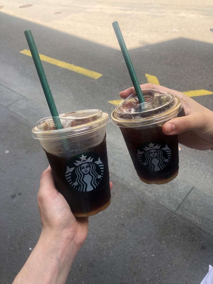 two people holding up starbucks drinks in their hands