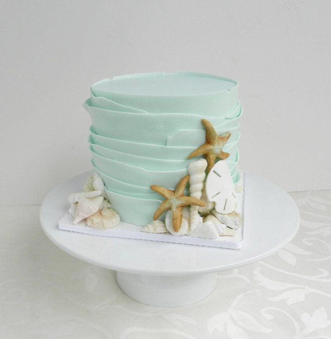 a stack of blue cups sitting on top of a white cake plate covered in sea shells