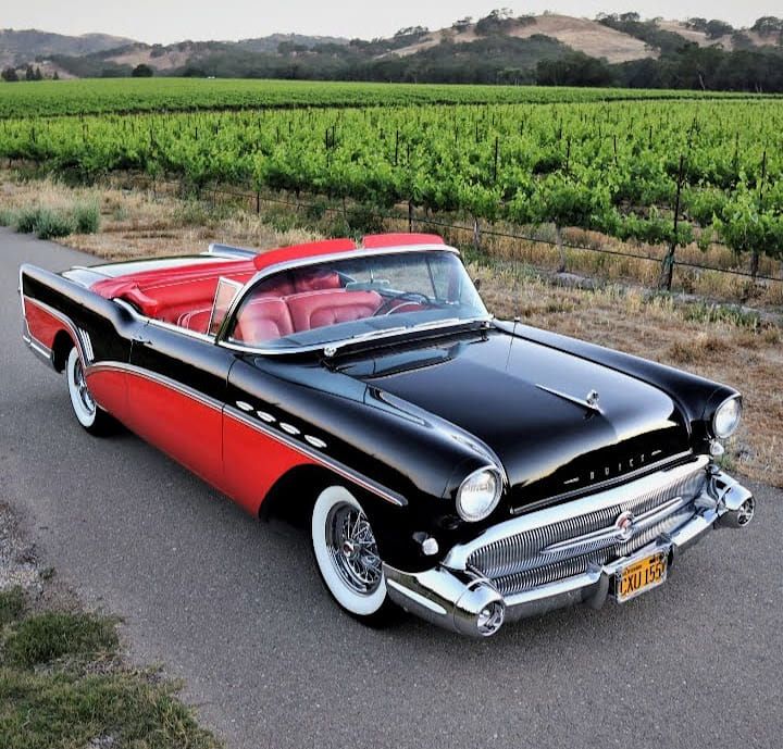 an old black and red car parked on the side of the road in front of a vineyard