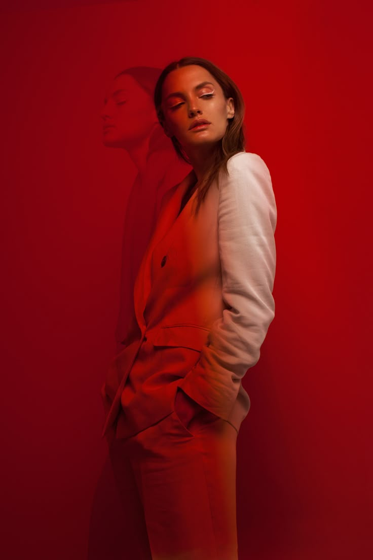 a woman standing in front of a red wall with her eyes closed and hands behind her back