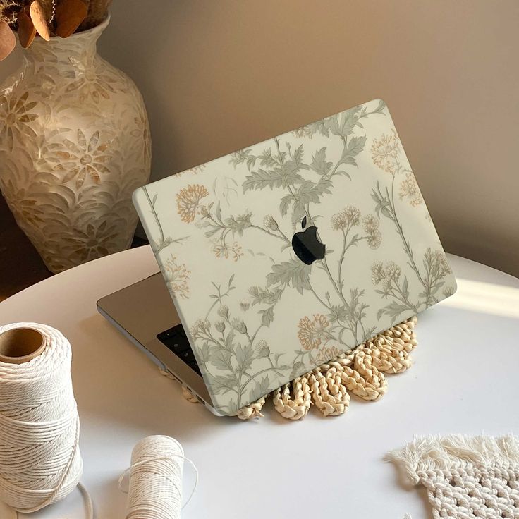 an apple laptop sitting on top of a table next to yarn and spools of thread