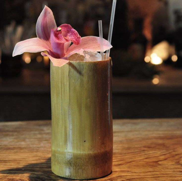 a drink with a flower in it sitting on a wooden table next to a candle