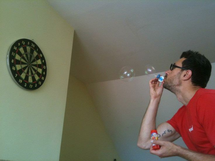 a man blowing bubbles into his mouth while standing in front of a dart and darts on the wall