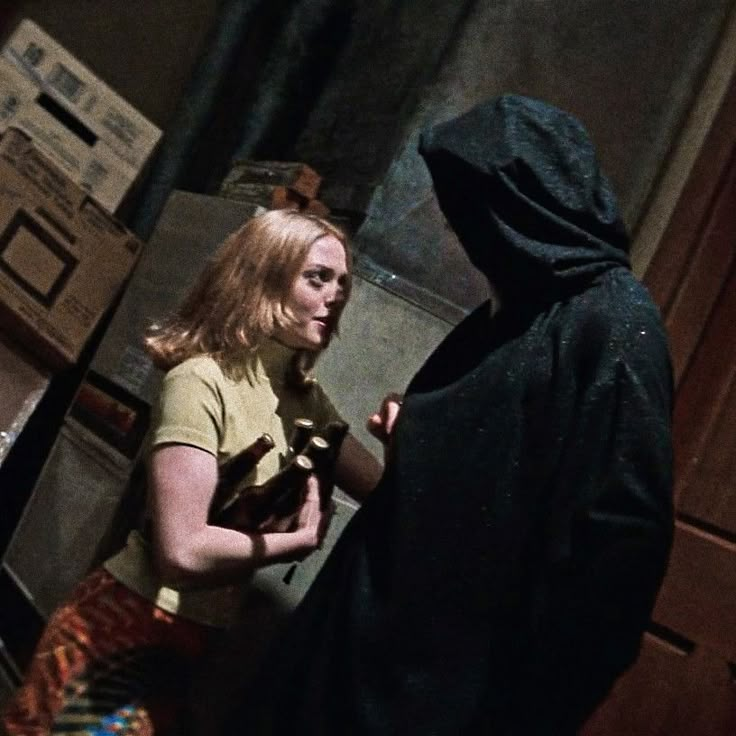 a woman standing next to a man in a dark room with boxes on the floor