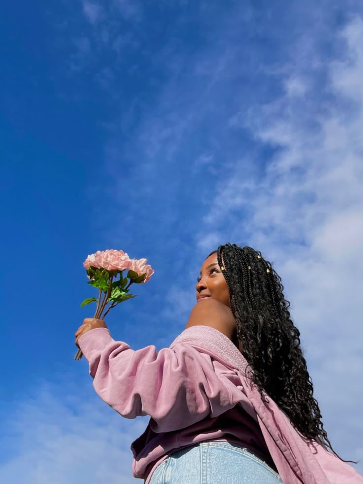 a woman holding a flower up in the air against a blue sky with white clouds