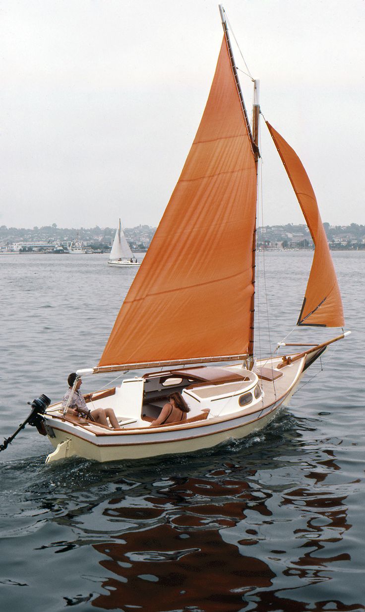 a small sailboat with orange sails in the water