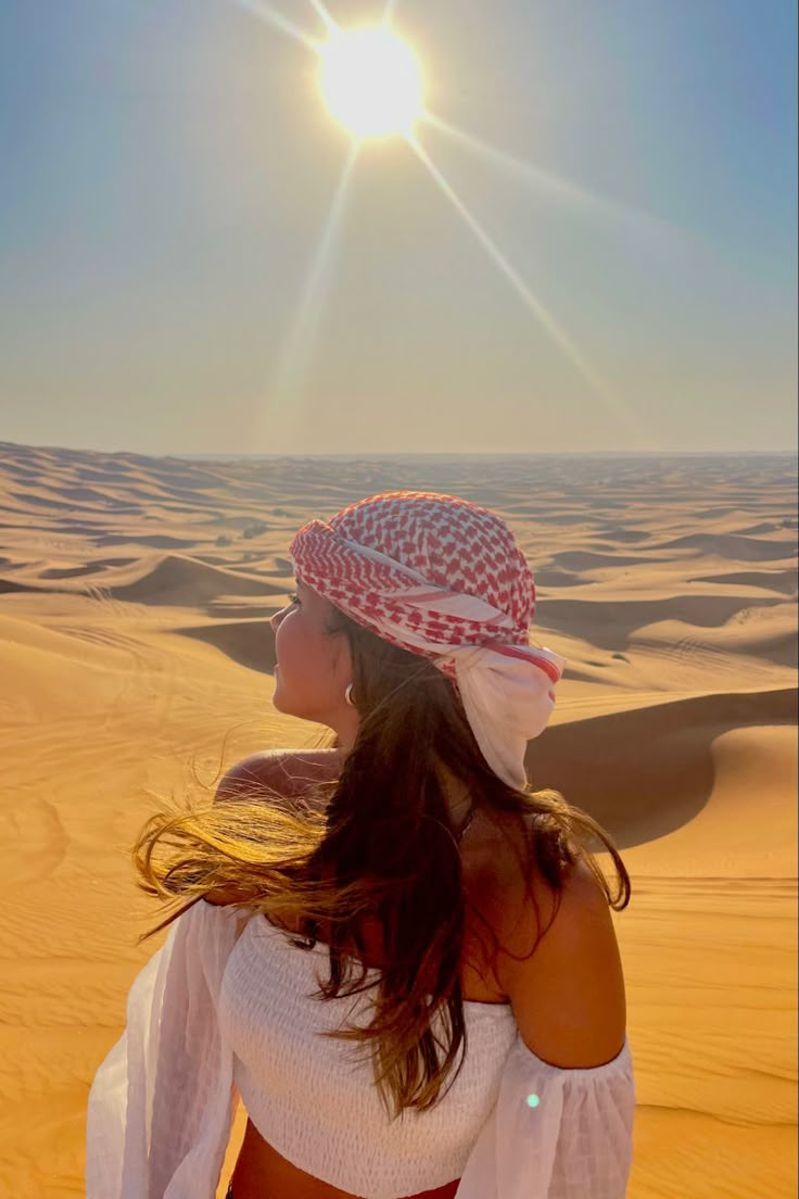 a woman standing in the desert with her hair blowing in the wind and sun behind her