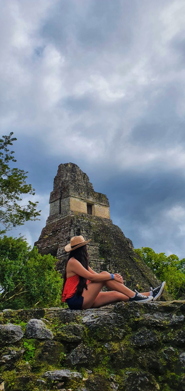 a woman sitting on top of a rock next to a tall tower under a cloudy sky