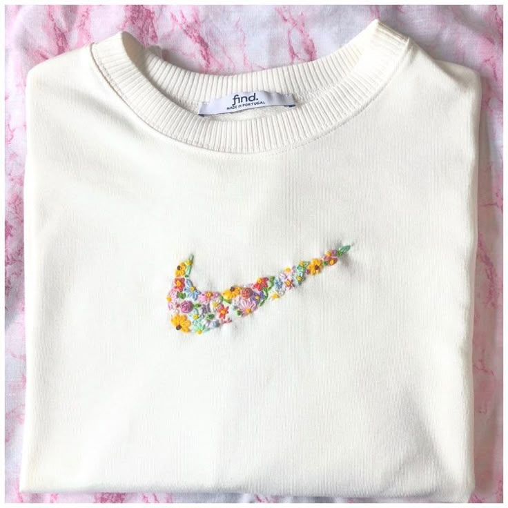 a white sweater with colorful beads on the front and back, sitting on a pink surface