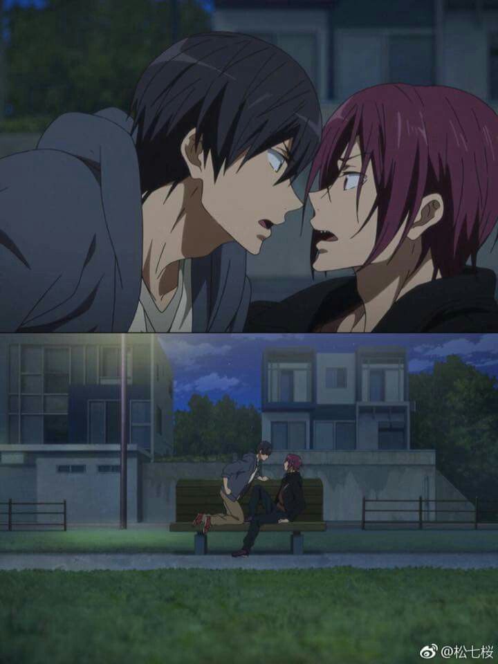 two people sitting on a bench in front of a building and one is kissing the other