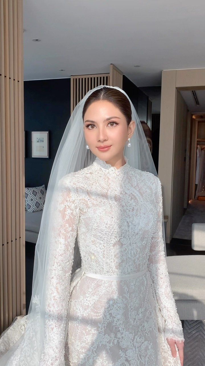 a woman in a white wedding gown and veil standing next to a bed with her hands on her hips