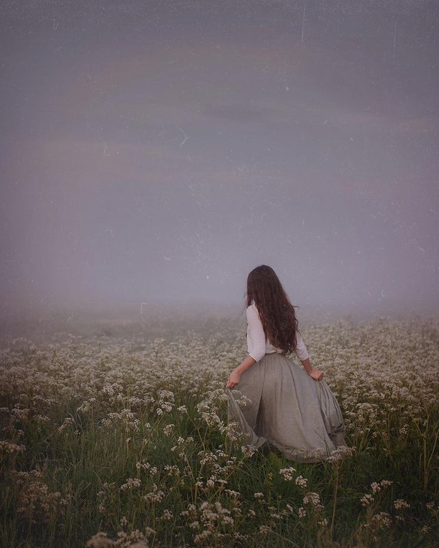 a woman sitting in the middle of a foggy field with her back to the camera