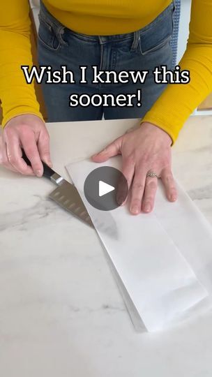 a woman cutting paper with a knife on top of a white counter next to a yellow shirt