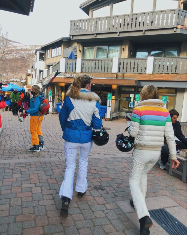 two women walking down the street in front of some buildings with snowboards on them