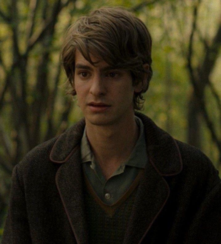 a young man standing in the woods looking at something to his left with trees behind him