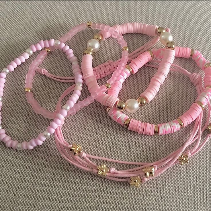 three pink bracelets with pearls and beads on a beige carpeted surface in front of a gray background