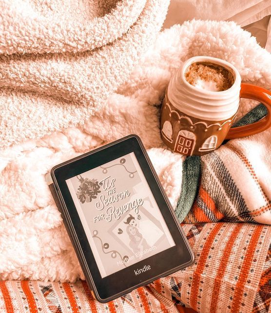 an electronic device sitting on top of a bed next to a cup of coffee and blanket