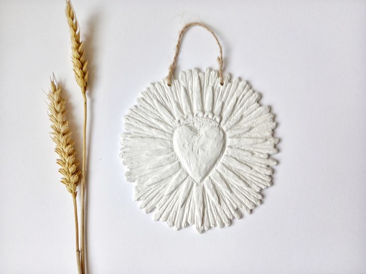 a white ceramic heart hanging on a wall next to two stalks of wheat, with the shape of a heart in the center