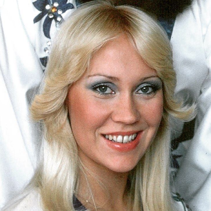 a woman with long blonde hair and blue eyes smiles at the camera while wearing a white jacket