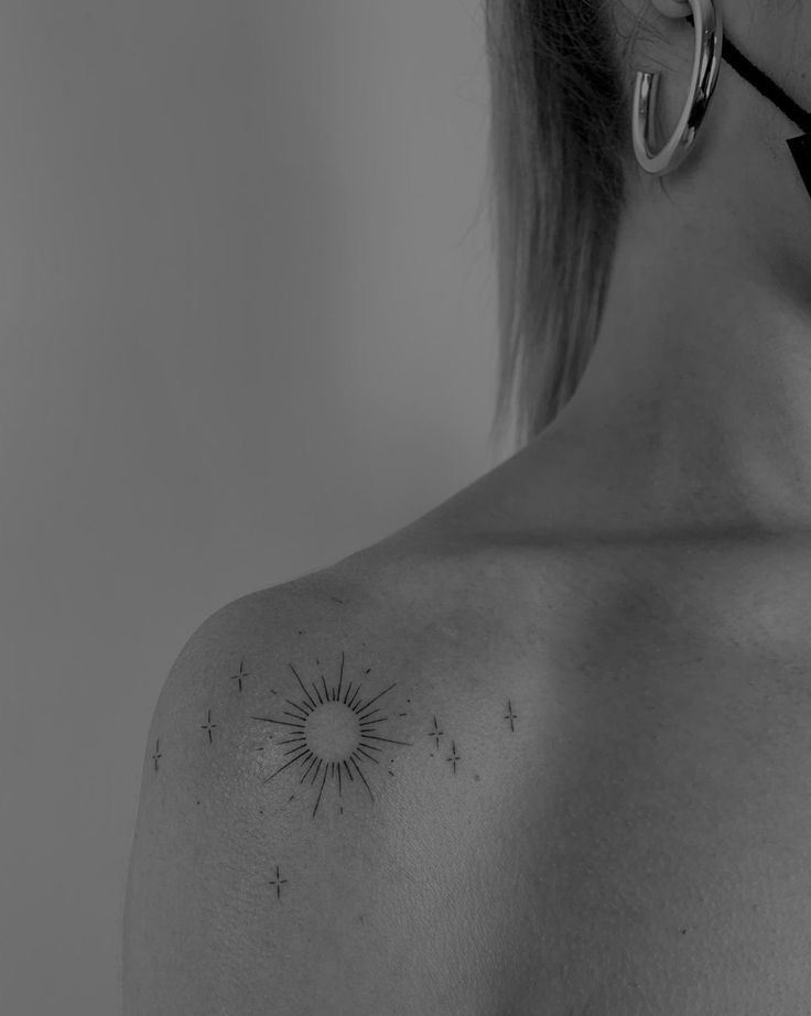 the back of a woman's shoulder with sun and stars tattoo on her left side