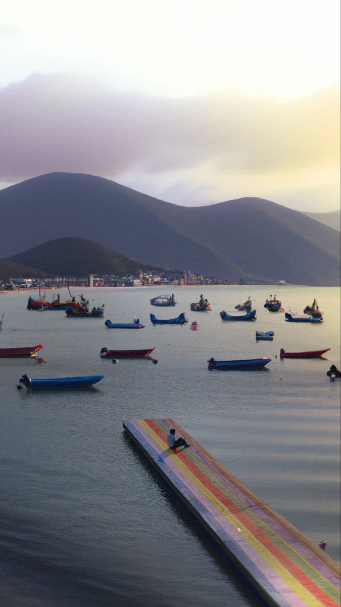 many boats floating in the water near mountains