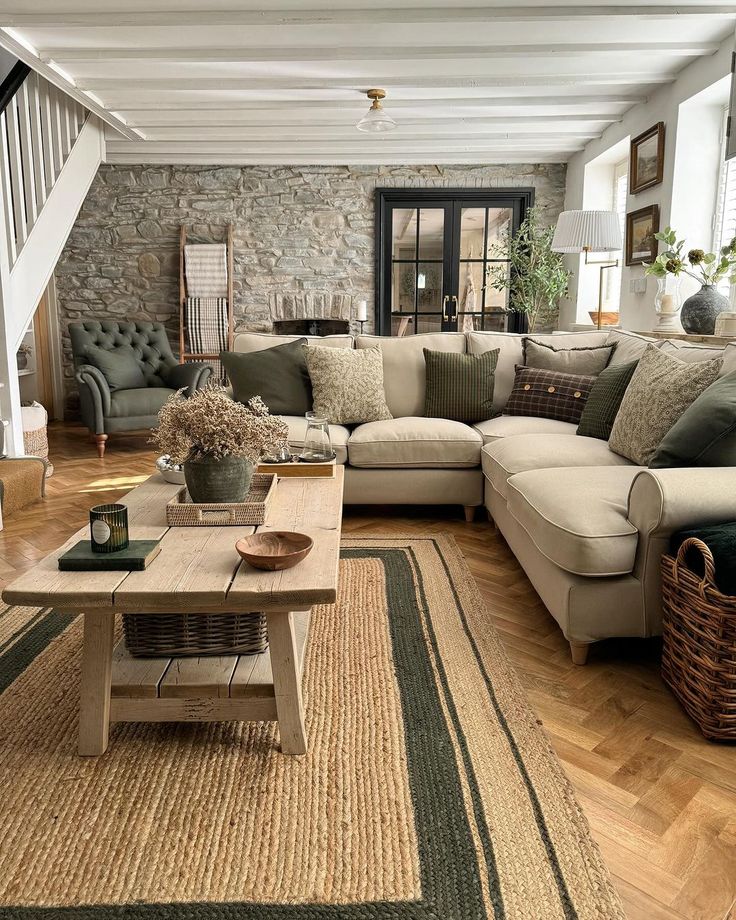 a living room filled with lots of furniture next to a stair case in front of a stone wall