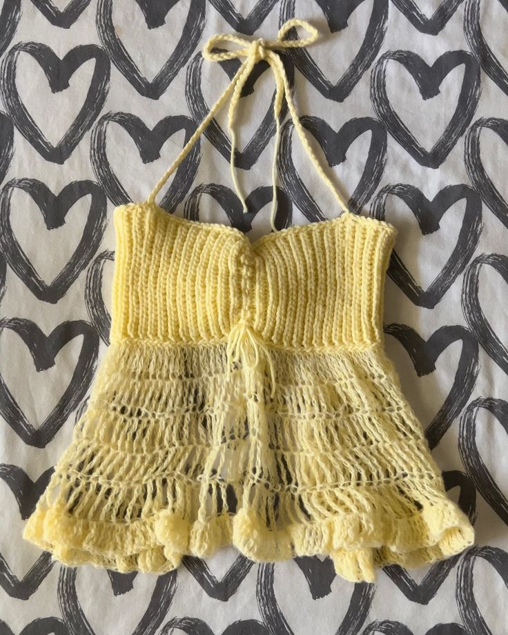 a crocheted yellow dress hanging on a black and white wallpaper with hearts in the background