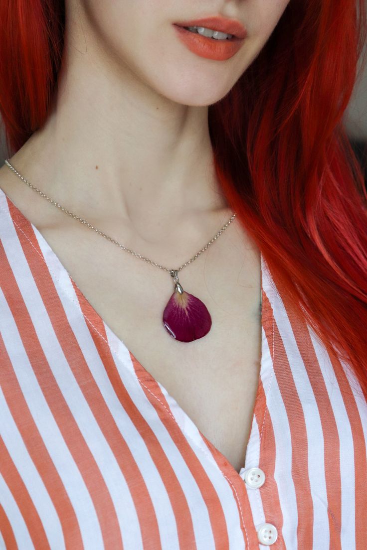 a woman with red hair wearing a striped shirt and a purple flower pendant on her necklace