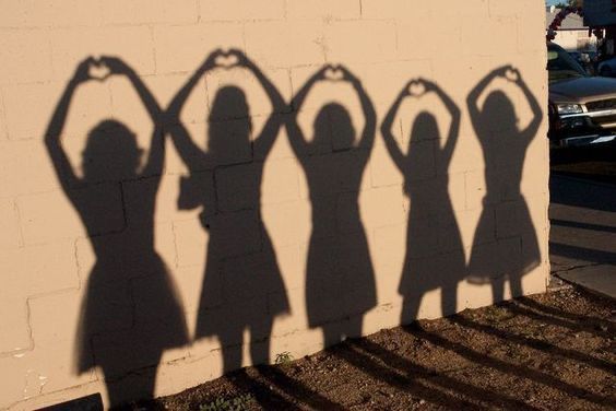 the shadow of four women standing in front of a wall with their hands on their hipss