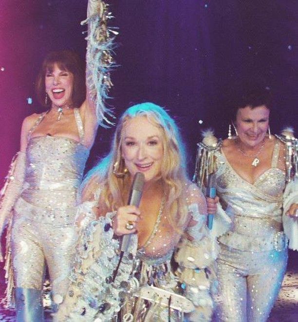 two women and one man are dressed in disco outfits while singing into a microphone on stage