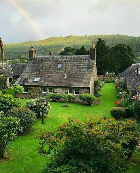 a house with a rainbow in the sky above it and some bushes on the ground