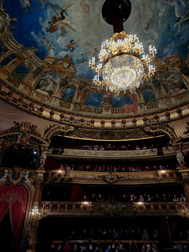 an ornately decorated auditorium with chandelier and paintings on the ceiling above it