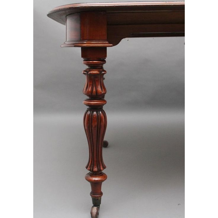 an antique wooden table with turned legs and wood grained finish on the top, against a gray background