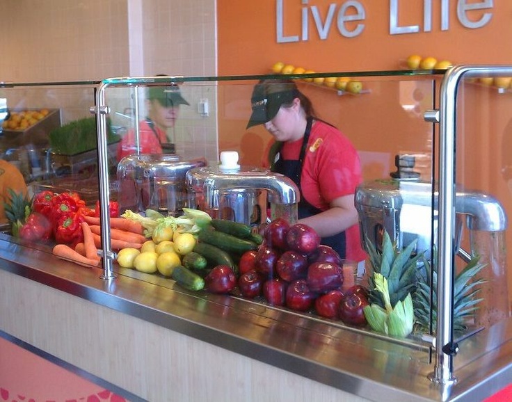 a woman standing behind a counter filled with fruits and vegetables