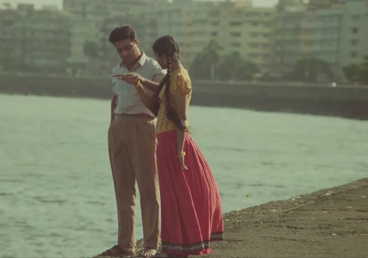 a man and woman standing next to the water looking at something on their cell phone