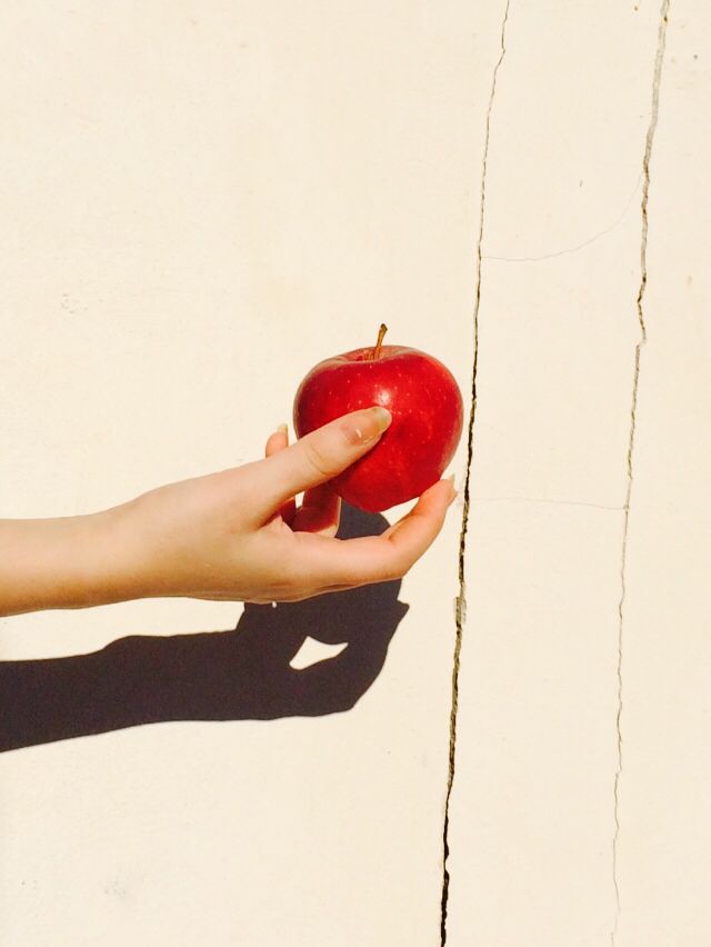 a person holding an apple in their hand with the shadow on it's wall