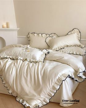 a bed with white sheets and ruffled edges in a room next to a fireplace