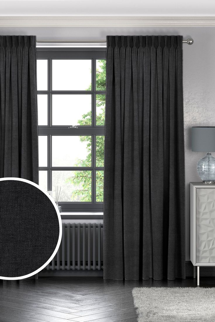 a black and white photo of a living room with grey curtains, dark wood flooring and a round mirror