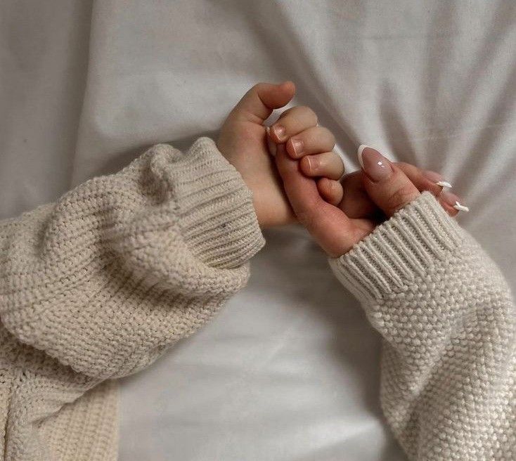 two hands holding each other while laying on top of a white bed covered in blankets