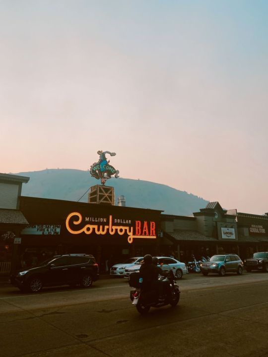 cars are parked in front of a building with a cowboy bar sign on it's roof