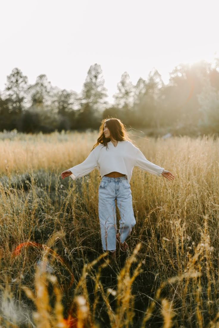 a woman standing in tall grass with her arms outstretched