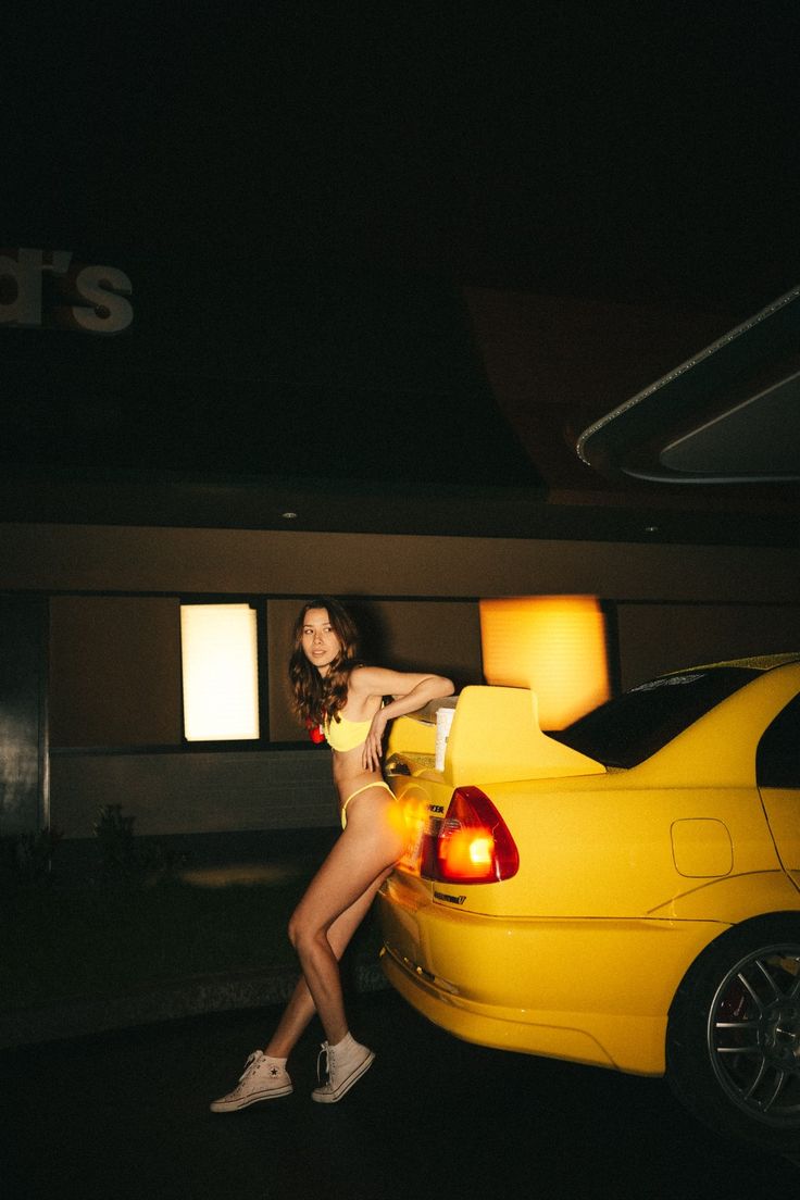 a woman leaning on the back of a yellow car