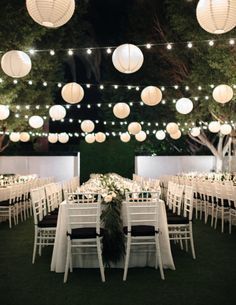 an outdoor wedding reception with paper lanterns and white tablecloths on the tables, surrounded by greenery