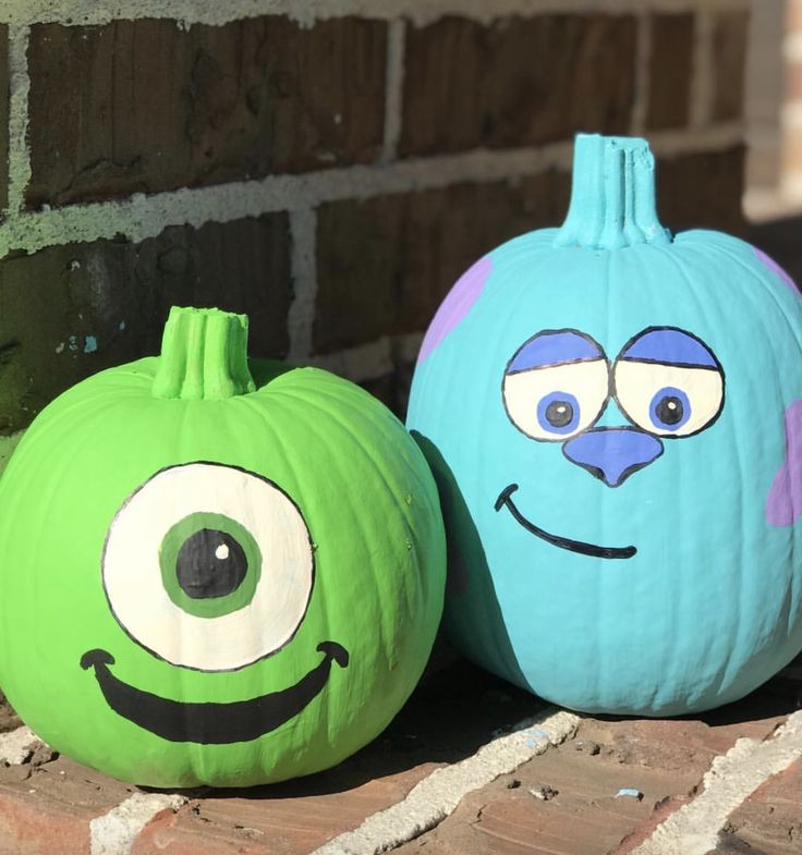 two pumpkins with faces painted on them are sitting in front of a brick wall