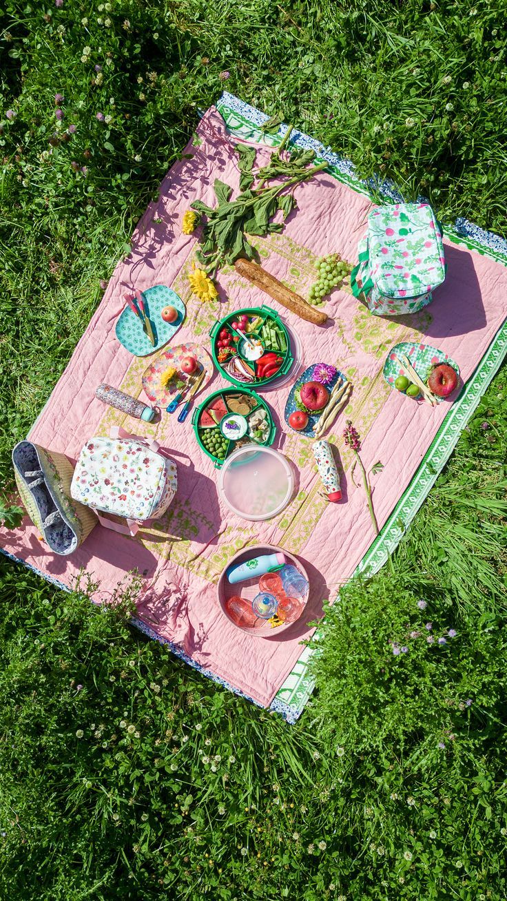 a picnic blanket is laid out on the grass with food and utensils in it