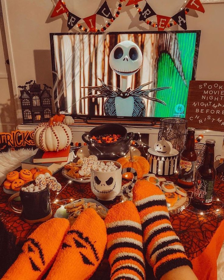 a person with their feet up on a table covered in halloween treats and decorations, watching tv