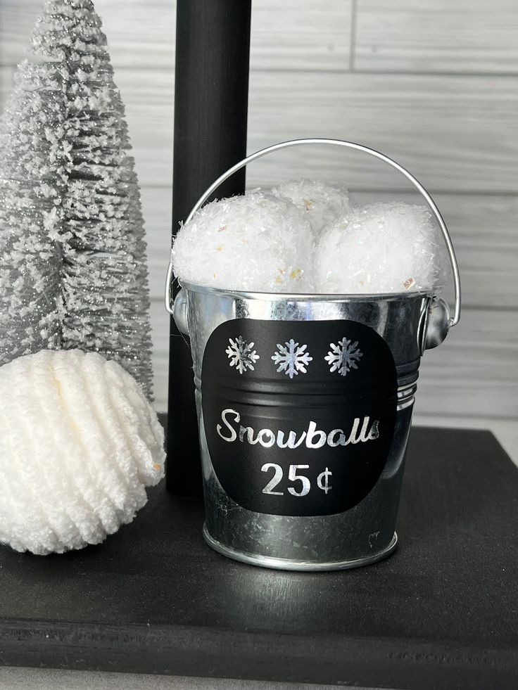 a bucket filled with white snowballs next to a christmas tree and a sign that says snowball 25 st