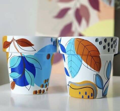 two colorful cups sitting on top of a white table next to each other with leaves painted on them