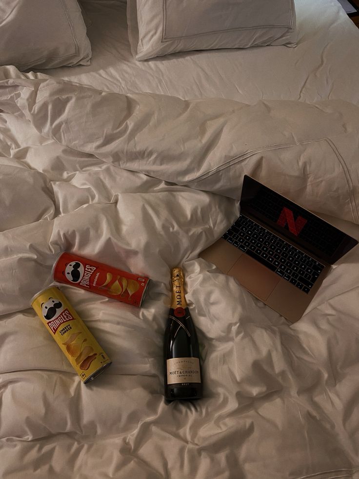 an open laptop computer sitting on top of a bed next to two bottles of wine