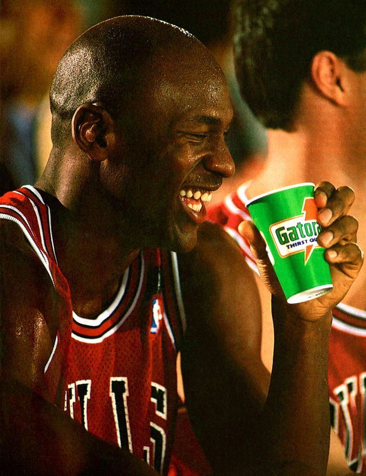 a man holding a green cup in his right hand and smiling while sitting next to other men